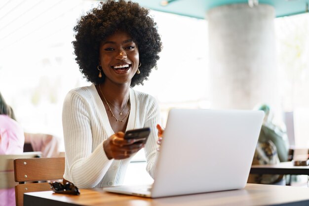 Sonriente joven africana sentada con una laptop en el café