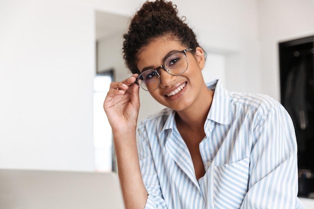 Sonriente joven africana trabajando en equipo portátil en la mesa en casa