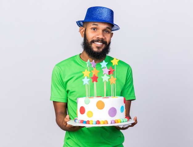 Sonriente joven afroamericano vistiendo gorro de fiesta sosteniendo la torta