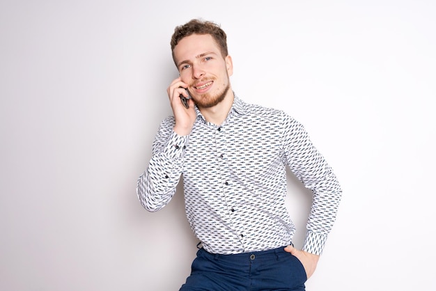 Sonriente joven apuesto hombre caucásico usando un teléfono inteligente para contactar a la familia