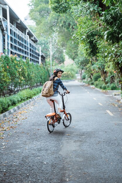 Sonriente joven asiática con casco y bolsa montar su bicicleta plegable