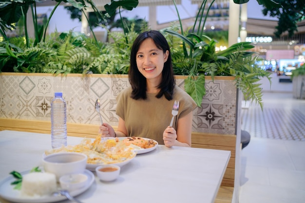 Sonriente joven asiática disfrutando de comidas como arroz frito americano y almejas fritas en un restaurante