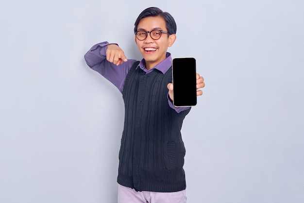 Sonriente joven asiático en camisa casual y chaleco mostrando teléfono móvil de pantalla en blanco recomendando aplicación móvil aislada sobre fondo blanco Concepto de estilo de vida de la gente