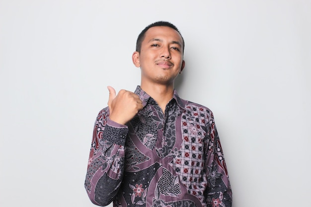 Sonriente joven asiático hombre vestido con camisa batik con pulgar arriba signo aislado sobre fondo blanco.
