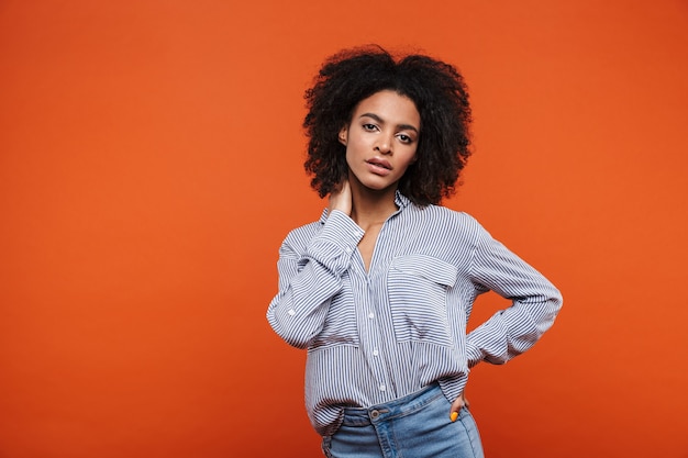 Sonriente joven atractiva mujer africana vistiendo ropa casual que se encuentran aisladas sobre la pared roja, posando