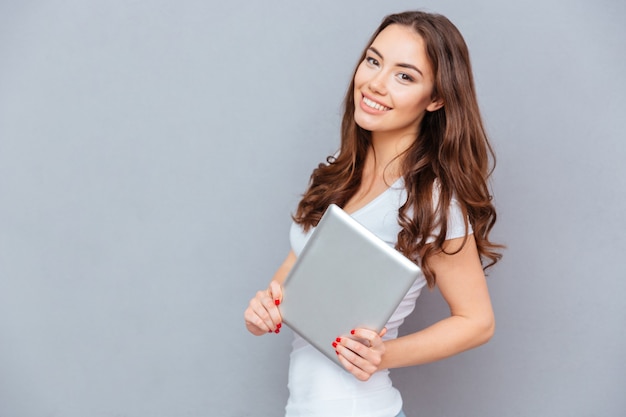 Sonriente joven atractiva de pie y sosteniendo la tableta