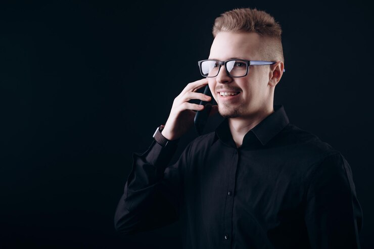 Sonriente joven barbudo en gafas hablando por teléfono inteligente