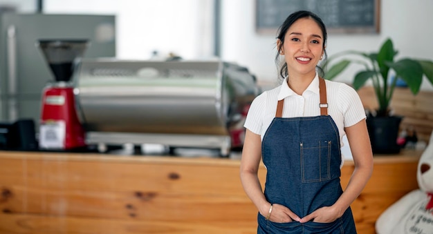 Foto sonriente joven barista asiática en delantal de pie en su café