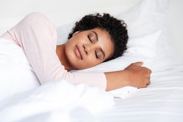 Sonriente joven y bella mujer africana tendido en la cama por la mañana, durmiendo