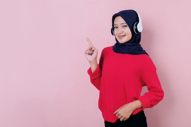 Sonriente a joven y bella mujer apuntando algo vistiendo camiseta roja con auriculares