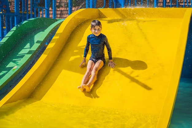 Sonriente joven cabalgando por un tobogán de agua amarillo