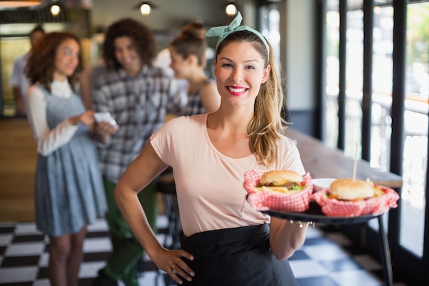 Sonriente joven camarera sirviendo hamburguesa en restaurante