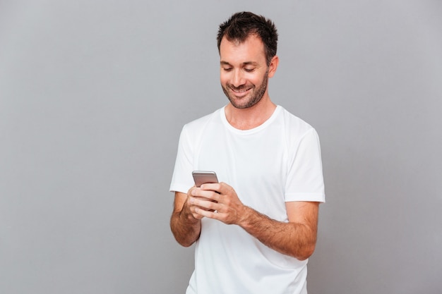 Sonriente joven con camisa blanca con smartphone sobre fondo gris