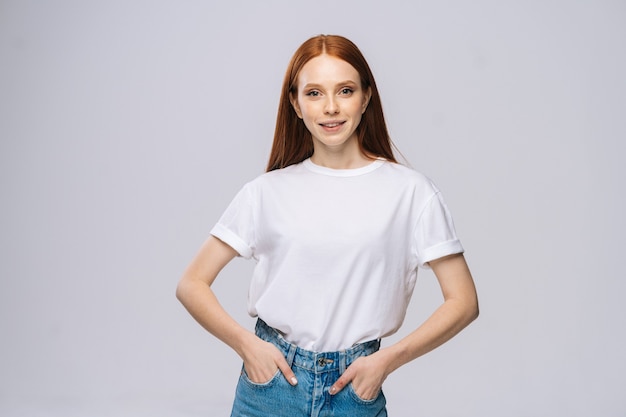 Sonriente joven en camiseta y pantalones de mezclilla tiene las manos en los bolsillos sobre fondo blanco aislado