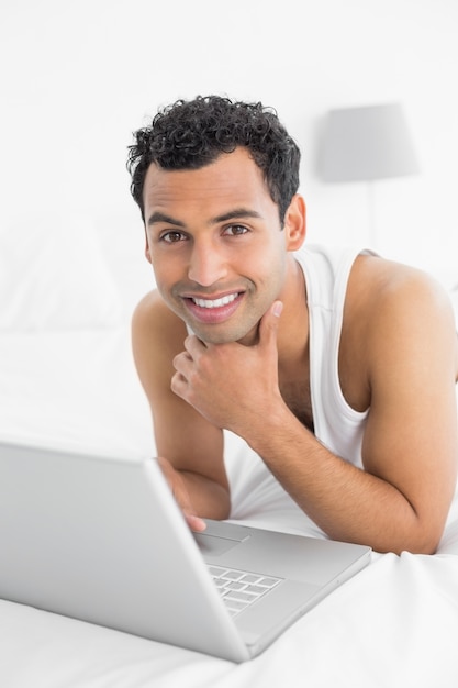 Sonriente joven casual con laptop en la cama