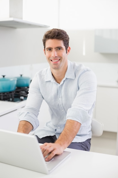 Sonriente joven casual con laptop en la cocina