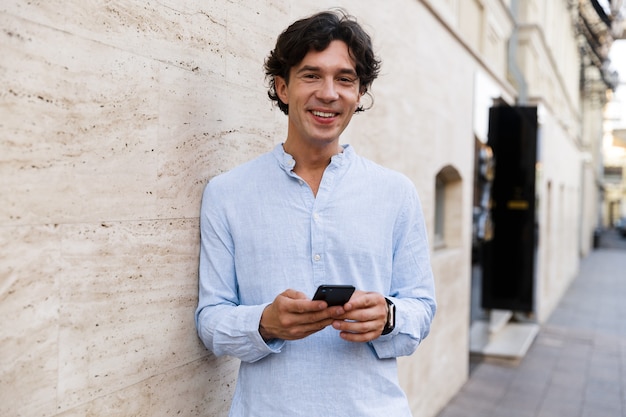 Sonriente joven casual sosteniendo teléfono móvil