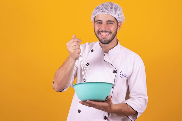 Sonriente joven chef masculino cocinero o panadero con camisa blanca uniforme posando aislado en un retrato de estudio de fondo amarillo Concepto de comida de cocina Mock up copy space Batir huevos batidos en un tazón