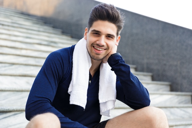 Sonriente joven deportista sentado en una escalera, descansando después de hacer ejercicio al aire libre