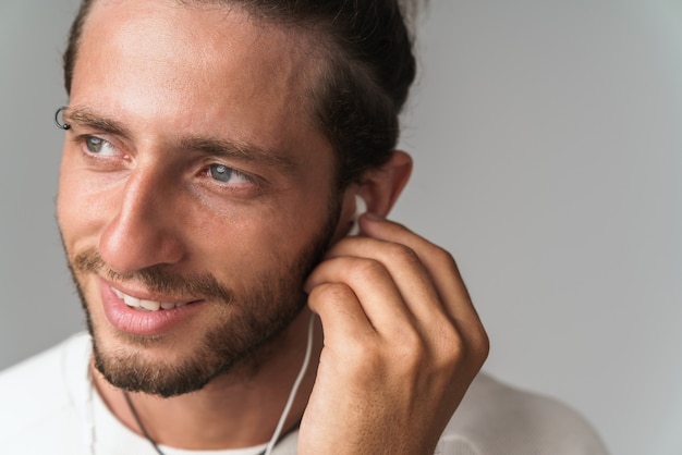 Sonriente joven disfruta escuchando música con auriculares mientras está de pie aislado en gris