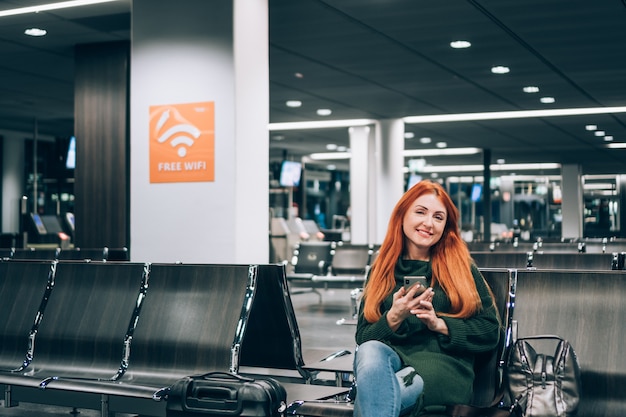 Sonriente joven disfruta de wi-fi gratuito en la terminal del aeropuerto