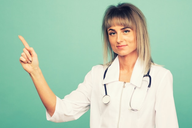 Sonriente joven doctora con un estetoscopio apunta sus dedos sobre un espacio azul