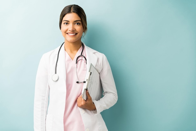 Foto sonriente joven doctora sosteniendo portapapeles mientras está de pie contra el fondo azul.