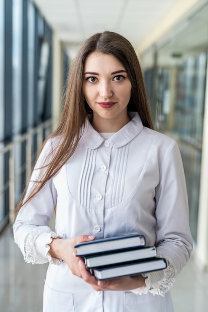 Sonriente joven doctora en uniforme con estetoscopio sosteniendo libro mientras está de pie