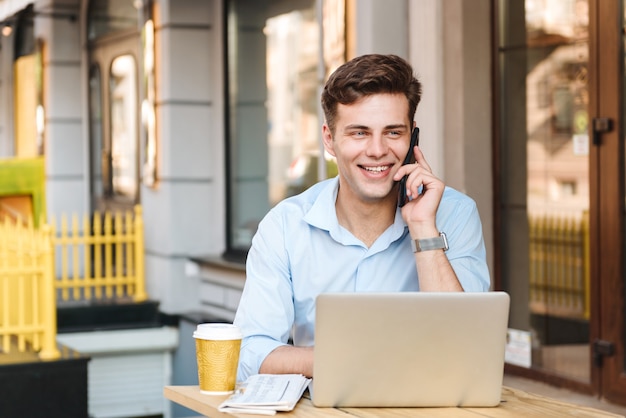 Sonriente joven elegante en camisa hablando por teléfono móvil