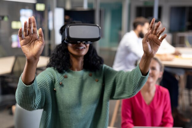 Sonriente joven empresaria afroamericana con simulador de realidad virtual haciendo gestos en la oficina