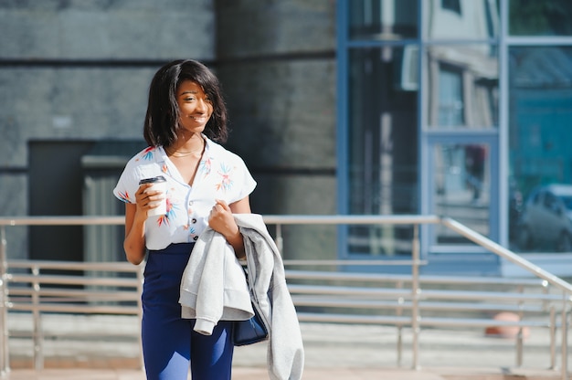 Sonriente joven empresaria afroamericana con taza de café en la ciudad