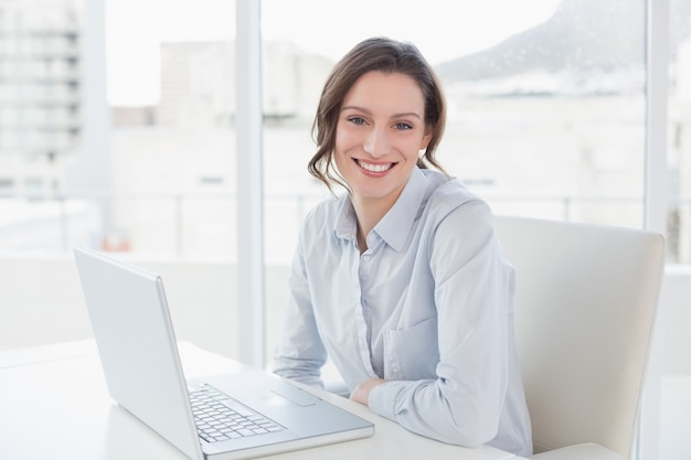 Sonriente joven empresaria con computadora portátil en la oficina