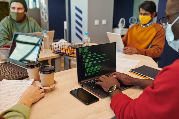 Sonriente joven empresaria en la pantalla del portátil mirando a un colega sentado junto al escritorio en la oficina de espacios abiertos durante la comunicación por video