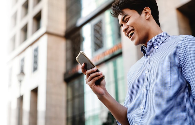 Sonriente joven empresario asiático mediante teléfono móvil en la ciudad