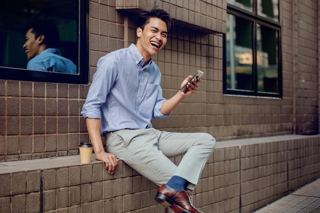 Sonriente joven empresario asiático mediante teléfono móvil en la ciudad