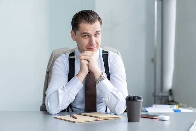 Sonriente joven empresario sentado en el escritorio, hablar por la cámara web, tener una videollamada o una conversación con el cliente, un entrenador o un entrenador masculino motivado, hablar, disparar, tutorial en línea, grabar un curso de capacitación