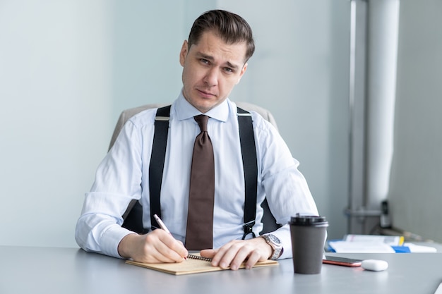 Sonriente joven empresario sentado en el escritorio, hablar por la cámara web, tener una videollamada o una conversación con el cliente, un entrenador o un entrenador masculino motivado, hablar, disparar, tutorial en línea, grabar un curso de capacitación