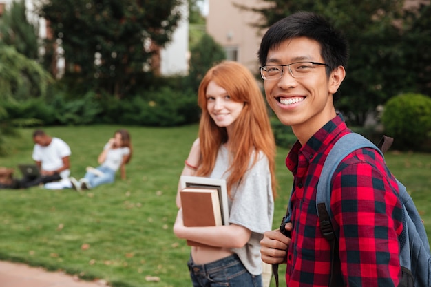Sonriente joven estudiante asiática con mochila caminando con su novia al aire libre