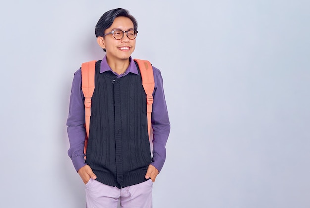 Sonriente joven estudiante masculino asiático de la universidad en ropa casual con una mochila de pie confiado en mirar a un lado aislado sobre fondo gris Educación en el concepto de colegio universitario de secundaria