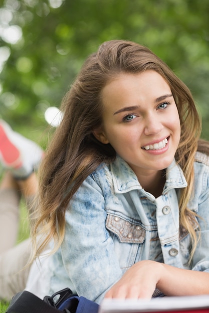 Sonriente joven estudiante tumbado en la hierba