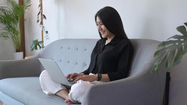 Sonriente joven freelancer que trabaja desde casa navegando en internet en una computadora portátil