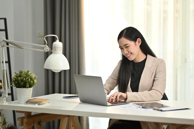 Sonriente joven gerente exclusiva con traje elegante revisando el correo electrónico de negocios en el monitor de la computadora portátil