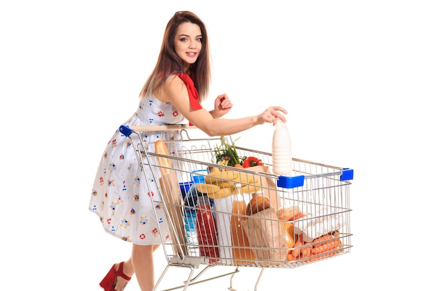 Sonriente joven haciendo compras en el supermercado ella está poniendo una botella de leche en el carro