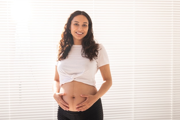 Sonriente joven hermosa mujer embarazada tocando su vientre y regocijándose concepto de positivo y