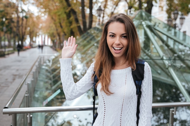 Sonriente joven hermosa saludando y saludando en el parque