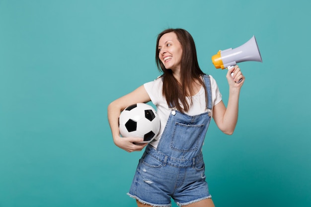 Sonriente joven hincha de fútbol apoya al equipo favorito con balón de fútbol, megáfono aislado en fondo azul turquesa. Emociones de la gente, concepto de estilo de vida de ocio familiar deportivo. Simulacros de espacio de copia.