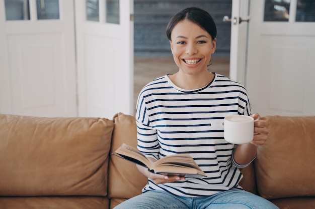 Sonriente joven hispana está leyendo el libro Literatura educación doméstica en cuarentena