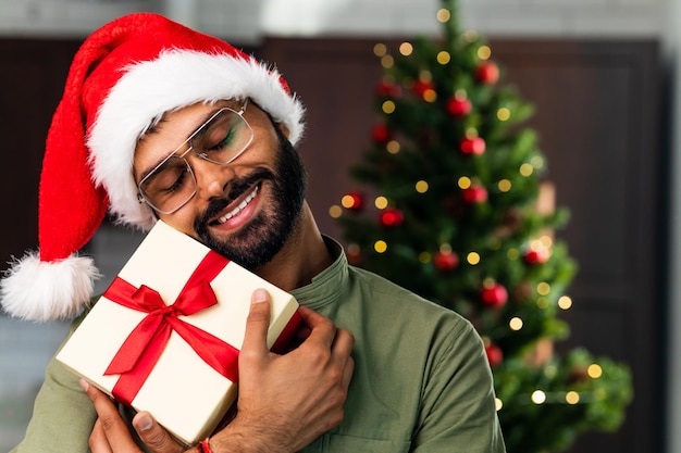 Sonriente joven hispano latino sosteniendo un regalo de Navidad en casa