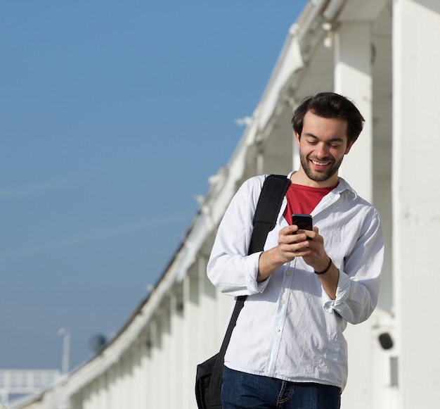 Sonriente joven leyendo mensajes de texto en el teléfono móvil