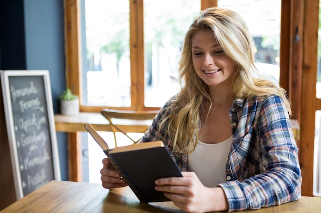 Sonriente joven libro de lectura en la mesa en la cafetería.